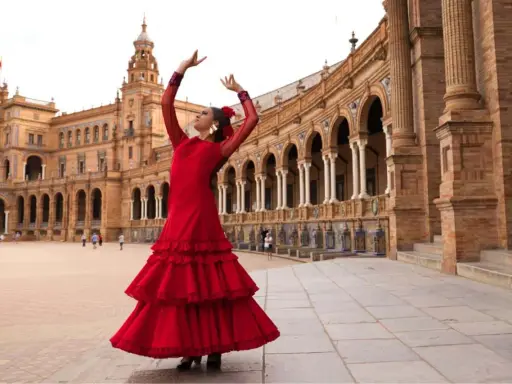 Una sevillana flamenca baila con pasión frente a un edificio histórico.