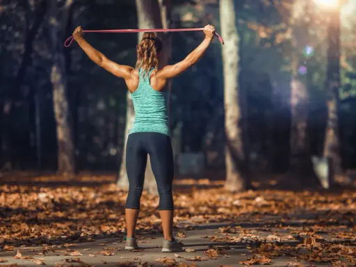 Mujer entrenando tren superior con tabla de ejercicios y gomas elásticas en un parque otoñal.