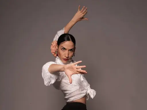 Bailarina de flamenco con flor en el pelo, ejecutando elegantes pasos de flamenco con expresión intensa.