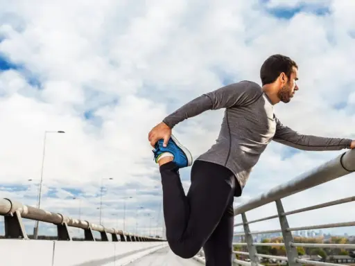 Hombre haciendo estiramientos antes de correr en un puente, con el cielo nublado de fondo.
