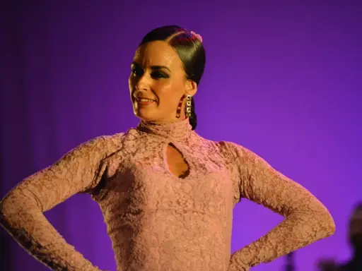 Bailaora de flamenco, con un vestido de encaje rosa, interpreta una seguiriya con pasión bajo luces púrpuras.