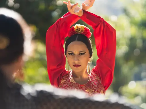 Mujer con traje rojo de flamenca, brazos en alto, mirando a otra persona.