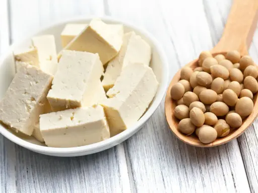 Tofu cortado en cubos en un bol blanco y una cuchara de madera llena de semillas de soja. ¿A qué sabe el tofu?