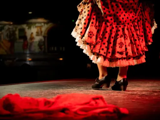 Pies de bailaora con volantes de lunares y flores, listos para un apasionado baile por bulerías.