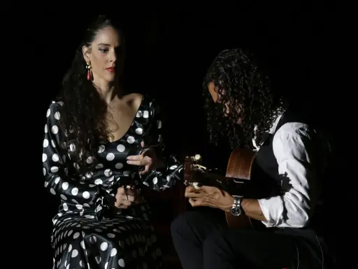Una bailaora flamenca con vestido de lunares y un guitarrista crean un duende que es pura pasión en la oscuridad.