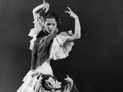 Una bailarina española famosa, con volantes y mantón, baila con gracia mientras una niña yace a sus pies.