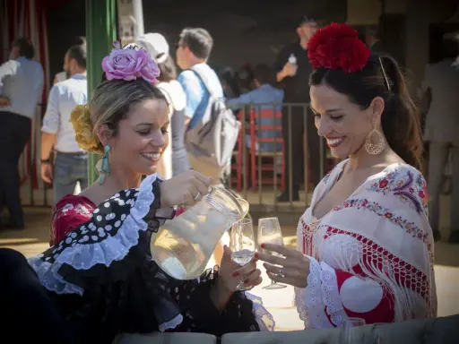 Dos mujeres con trajes de flamenca, una sirviendo bebida. Un vistazo a la historia del traje de flamenca.