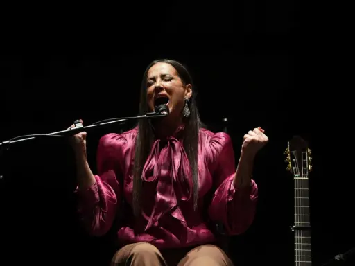Cantante flamenco mujer, con el alma desbordada, canta apasionadamente frente al micrófono. A su lado, una guitarra espera.