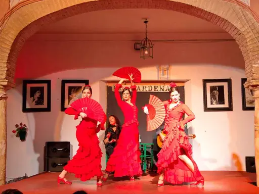 Tres bailarinas de flamenco, vestidas de rojo y con abanicos, ejecutan fandangos flamencos en un escenario.