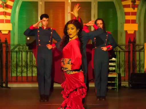 Una bailaora de flamenco con un vestido rojo vibrante, rodeada por dos hombres con uniformes militares, capturando la esencia de las alegrías flamenco.