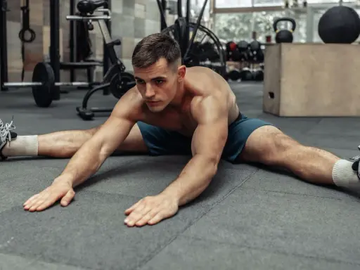 Hombre haciendo estiramiento de piernas en el suelo, preparándose para el calentamiento antes de entrenar.