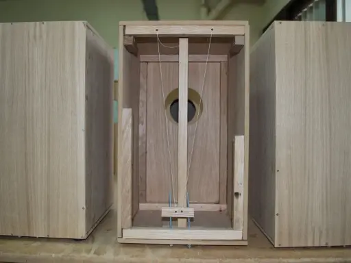 Partes de un cajón de madera, mostrando la estructura interna con cuerdas y un agujero circular.