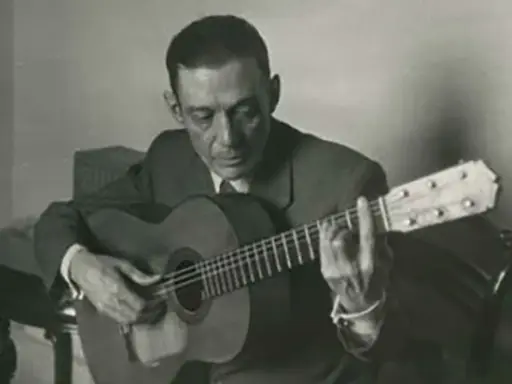 Un guitarrista flamenco andaluz, con traje y corbata, toca su guitarra con pasión.