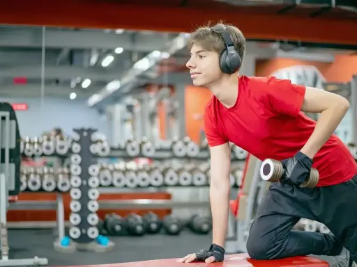 Joven con auriculares entrena en gimnasio. ¿Hacer pesas a los 15 años detiene mi crecimiento?