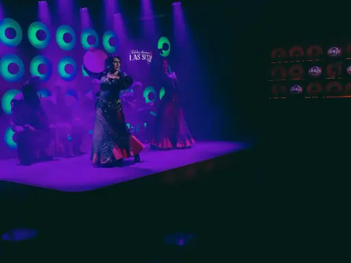 Dos bailarinas de danza sevillana, con trajes vibrantes, actúan bajo luces púrpuras y verdes.