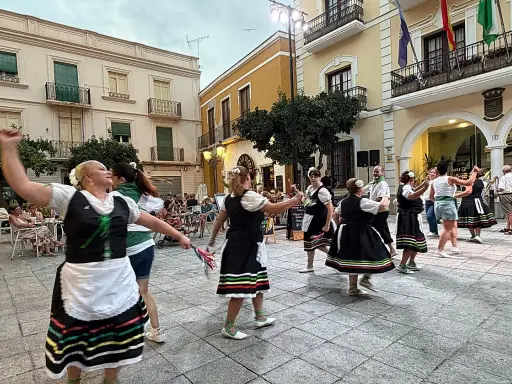 Un grupo de mujeres realiza un animado fandango dance en una plaza, vestidas con trajes tradicionales.
