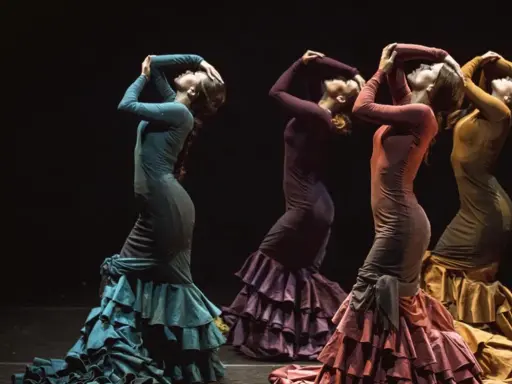 Cuatro mujeres flamencas bailando con vestidos de volantes en tonos tierra.