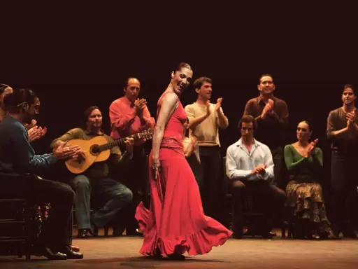 Bailaora flamenca en vestido rojo, acompañada por guitarrista y palmas. Un espectáculo de mejor flamenco.