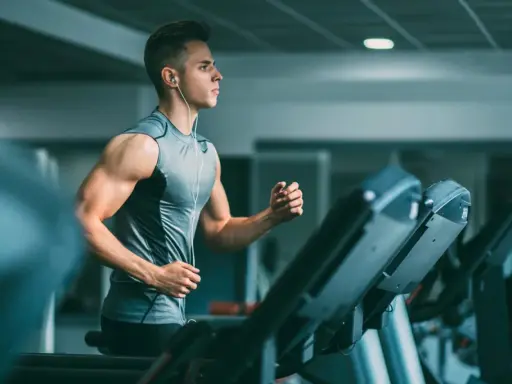 Joven con audífonos haciendo liss cardio en una cinta de correr en el gimnasio.