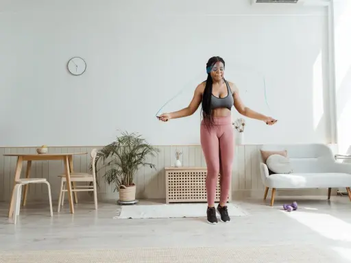 Mujer joven con auriculares realiza ejercicio hit saltando la cuerda en su sala de estar.