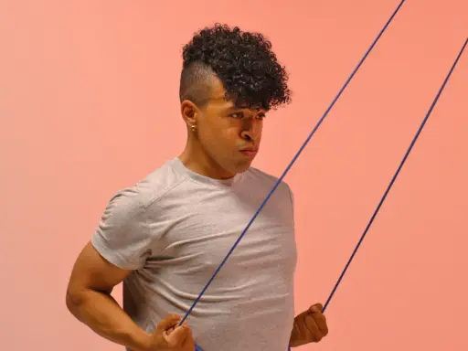 Hombre con cabello rizado haciendo ejercicio con banda elástica para mejorar la movilidad tren superior.