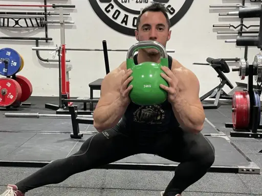Hombre realiza desplantes laterales con pesa rusa verde en un gimnasio.