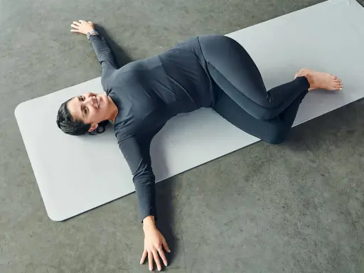 Mujer sonriente practicando ejercicios de yoga para relajarse, en posición de torsión acostada.