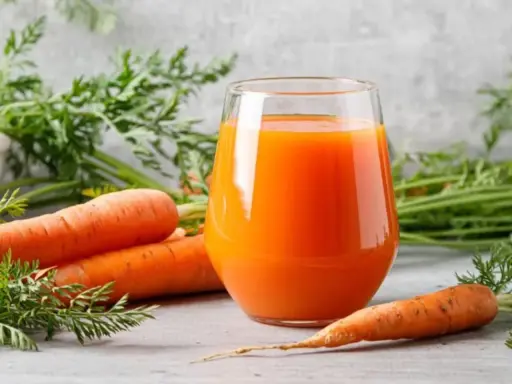 Un vaso de jugo de zanahoria fresco junto a zanahorias enteras. Descubre para qué es buena la zanahoria: ¡salud y vitalidad!