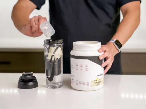 Hombre prepara batido con proteína en polvo para ganar músculo. El envase indica para qué sirve la proteína en polvo: energizar y recuperación post-entreno.