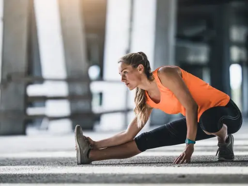 Mujer haciendo calentamiento antes de correr, estirando la pierna izquierda en un entorno urbano.