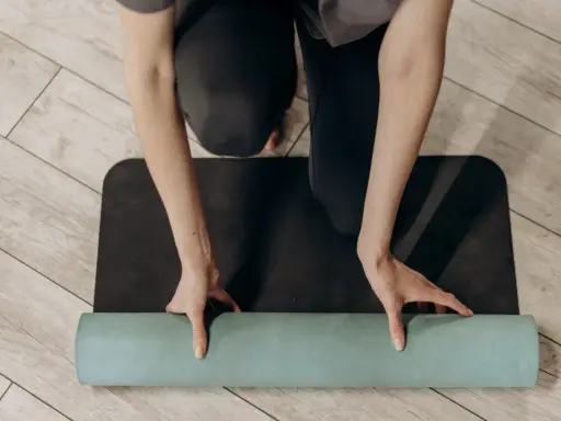 Manos enrollando una esterilla de yoga verde sobre una esterilla negra. Un paso esencial para saber como limpiar esterilla yoga y mantenerla en buen estado.