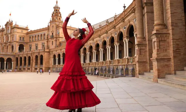 Una sevillana flamenca baila con pasión frente a un edificio histórico.