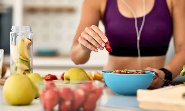 Mujer en ropa deportiva prepara su desayuno saludable con frutas frescas, pensando en qué desayunar antes de entrenar.