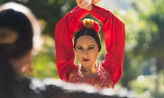 Mujer con traje rojo de flamenca, brazos en alto, mirando a otra persona.