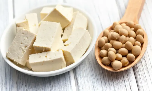 Tofu cortado en cubos en un bol blanco y una cuchara de madera llena de semillas de soja. ¿A qué sabe el tofu?