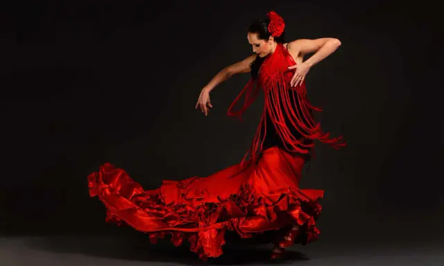 Bailarina de flamenco con vestido rojo voluminoso y mantón de flecos. Un ejemplo de las curiosidades del flamenco, su pasión y elegancia.