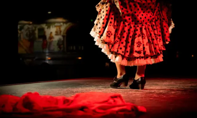 Pies de bailaora con volantes de lunares y flores, listos para un apasionado baile por bulerías.