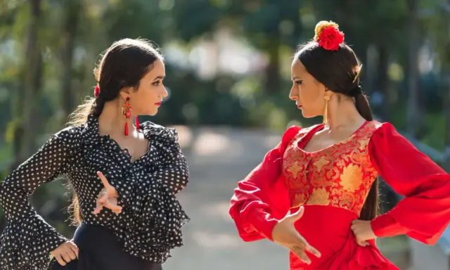 Dos mujeres practican baile flamenco para principiantes en un parque, una con traje de lunares y otra de rojo vibrante.