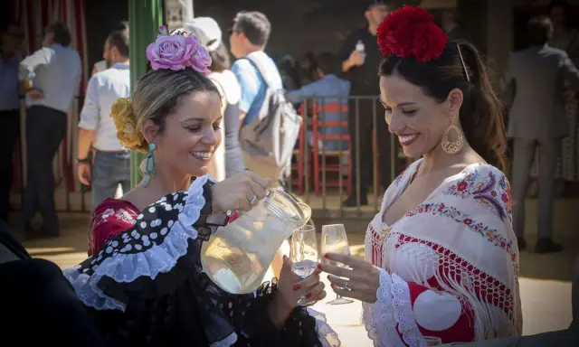 Dos mujeres con trajes de flamenca, una sirviendo bebida. Un vistazo a la historia del traje de flamenca.
