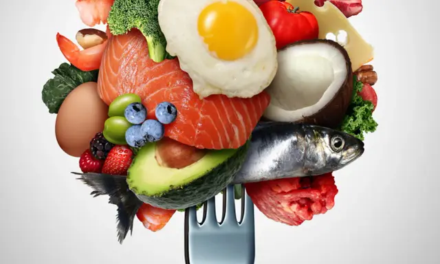 Un tenedor carga una variedad de alimentos saludables, incluyendo salmón, aguacate, huevo, bayas y verduras bajas en carbohidratos, ideal para una dieta equilibrada.