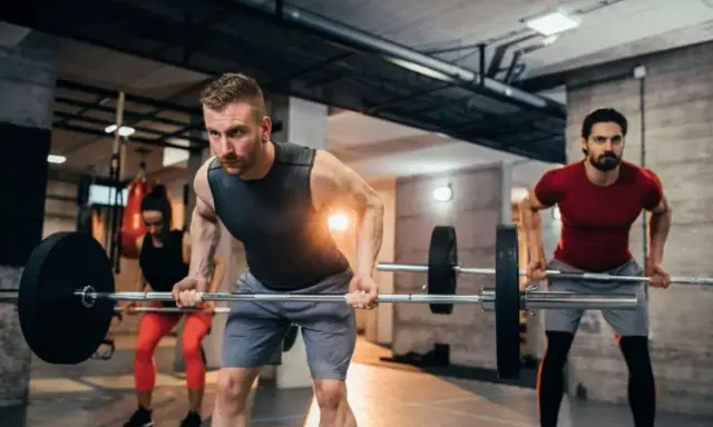 Hombres y mujeres realizando ejercicios de espalda en el gym con barras.