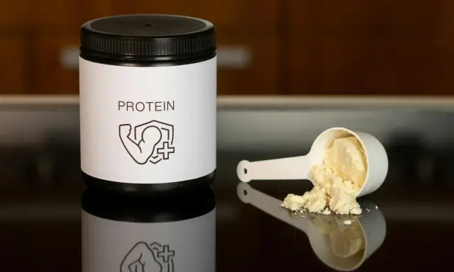 Un bote de proteína y una cuchara con polvo. Ideal para saber como tomar proteína y potenciar tus entrenamientos.