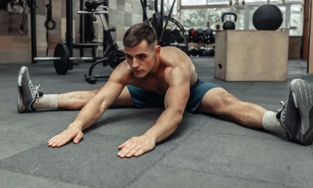 Hombre haciendo estiramiento de piernas en el suelo, preparándose para el calentamiento antes de entrenar.