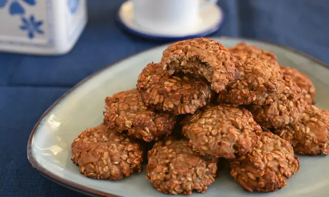Montón de galletas proteicas caseras en un plato, con una taza de café al fondo. ¡Una deliciosa receta de cookies proteicas!