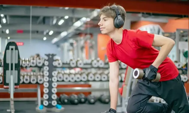 Joven con auriculares entrena en gimnasio. ¿Hacer pesas a los 15 años detiene mi crecimiento?