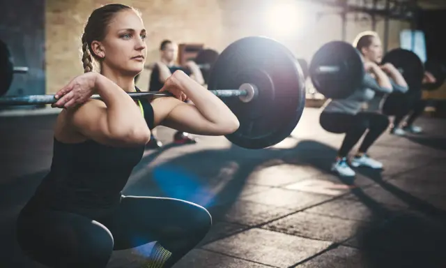 Mujeres realizando sentadillas con barra, un ejemplo de ejercicios compuestos en el gym.