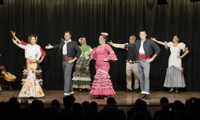 Artistas de sevillanas y flamenco en escena, con trajes coloridos y movimientos apasionados.