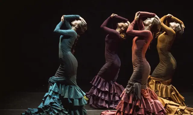 Cuatro mujeres flamencas bailando con vestidos de volantes en tonos tierra.