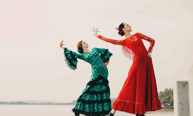 Dos bailarinas de flamenco, una con vestido verde de lunares y otra con rojo vibrante, ejecutan un apasionado flamenco ballo.