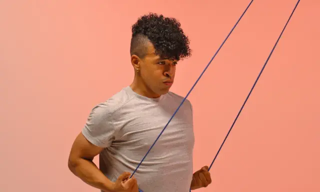 Hombre con cabello rizado haciendo ejercicio con banda elástica para mejorar la movilidad tren superior.